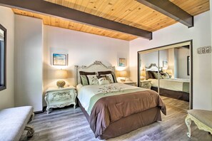Quarto com uma cama grande, duas mesas de cabeceira, um espelho e teto de madeira.