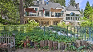A large house with a covered porch, a flag, and a wooden fence. - Waterfront Lake Arrowhead Home w/ View & Game Room (Lake Arrowhead)