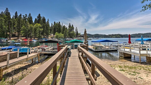 A wooden dock leading to a marina with boats and a forested hillside in the background. - Waterfront Lake Arrowhead Home w/ View & Game Room (Lake Arrowhead)