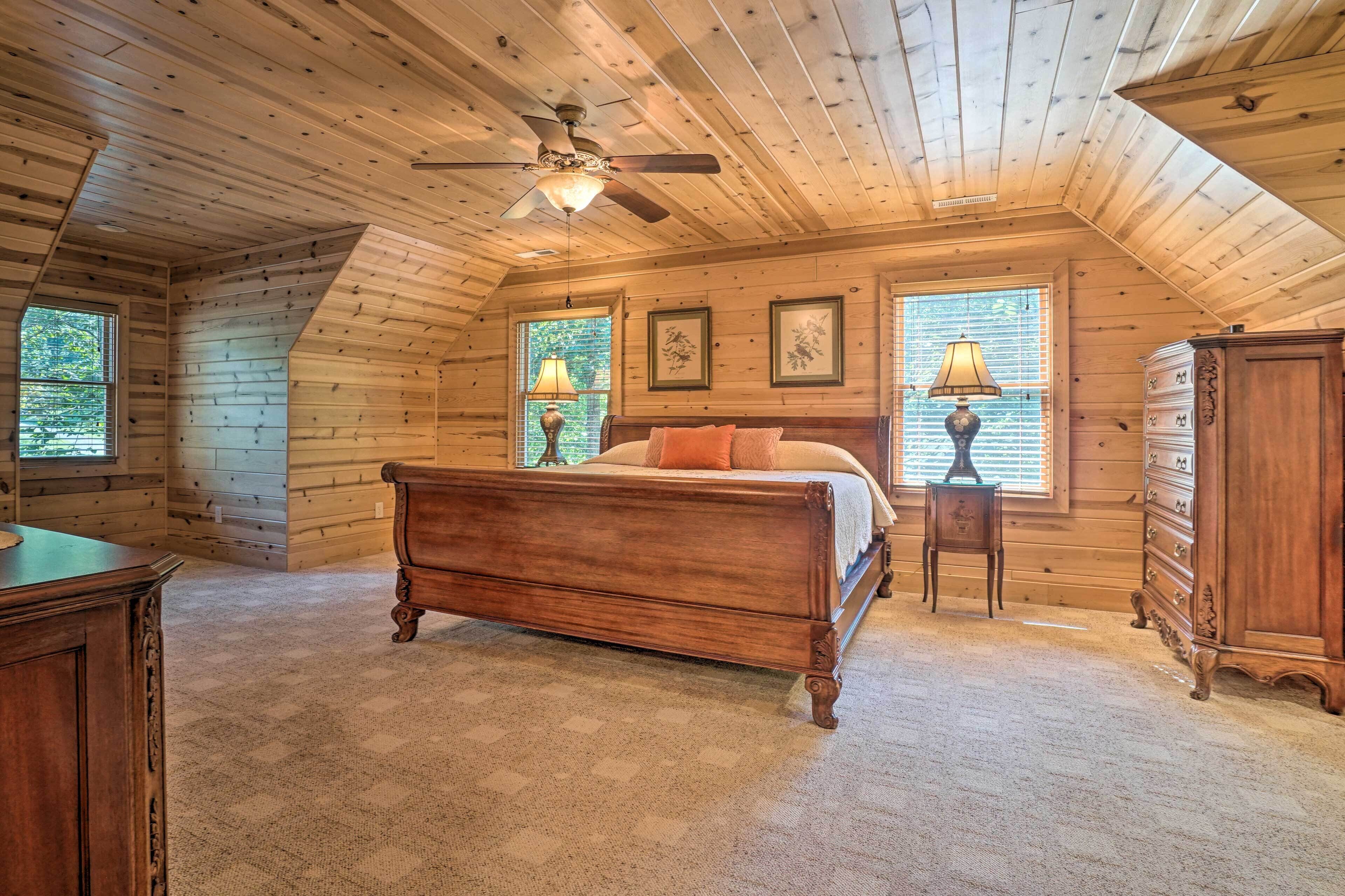 A bedroom with a wooden ceiling, a bed, a dresser, and two windows with lamps.