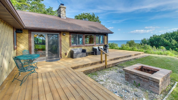 Una terraza de madera con mobiliario exterior, un hogar para fuego y vista al océano.