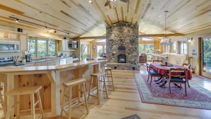 Cocina amplia con encimeras de madera y taburetes de bar, chimenea de piedra y comedor con alfombra roja.