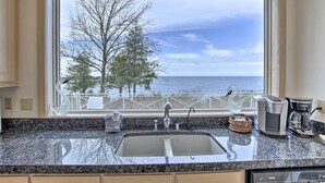 A kitchen with a granite countertop, a sink, a coffee maker, and a view of the sea through a window. - Grand Egg Harbor Home w/ Stunning Lake Views! (Egg Harbor)