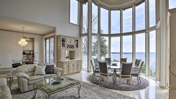 A spacious living room with a large bay window, a dining area with a round table and chairs, and a kitchen area with cabinets and a chandelier. - Grand Egg Harbor Home w/ Stunning Lake Views! (Egg Harbor)