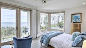 A bedroom with a large bed, a chair, a desk, and a view of the sea. - Grand Egg Harbor Home w/ Stunning Lake Views! (Egg Harbor)