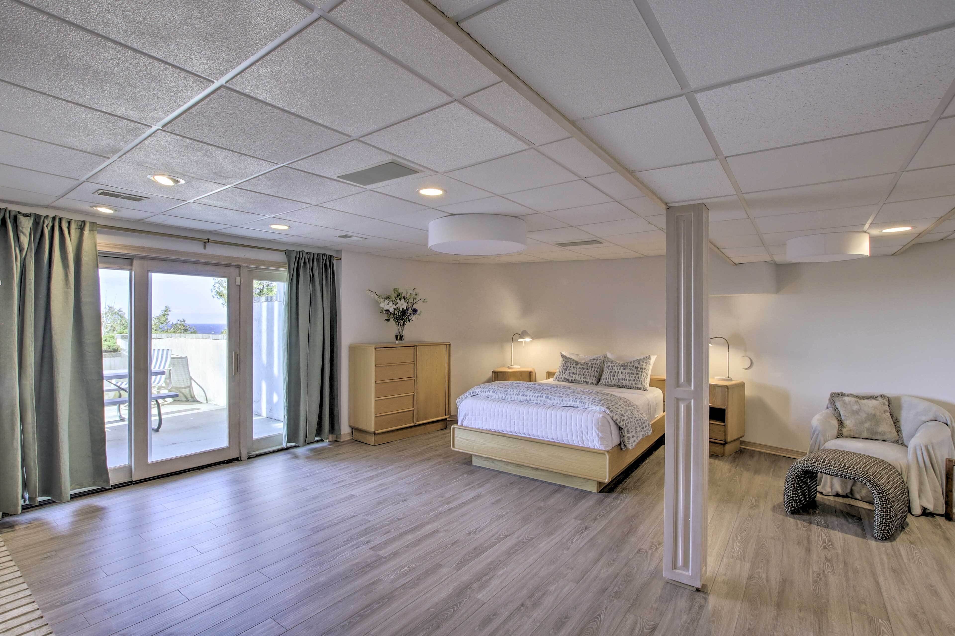 Un dormitorio amplio con una cama grande, una mesita de noche, un aparador y vistas al exterior a través de una puerta corrediza de vidrio.