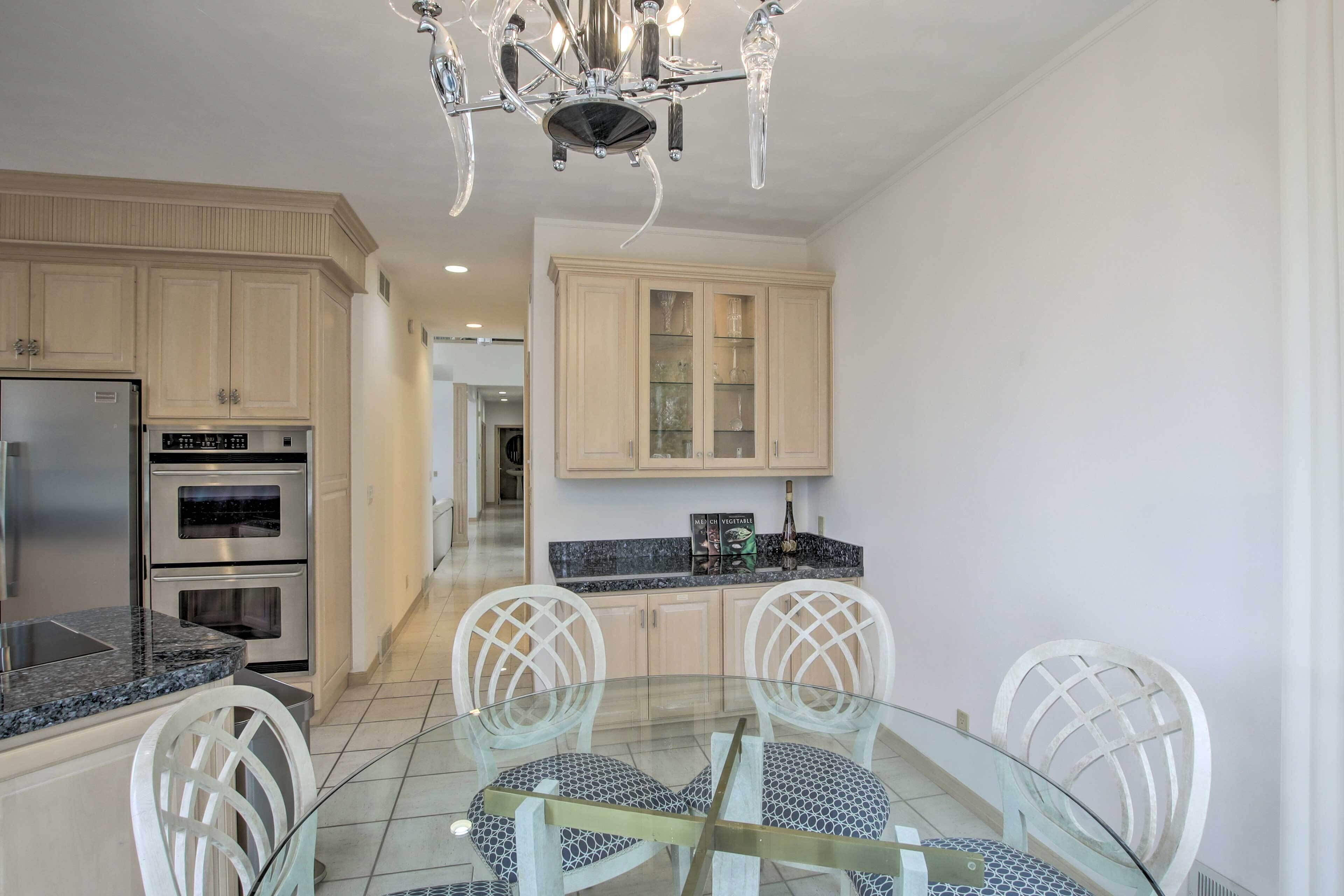 A modern kitchen with built-in appliances, a glass dining table, and white chairs.