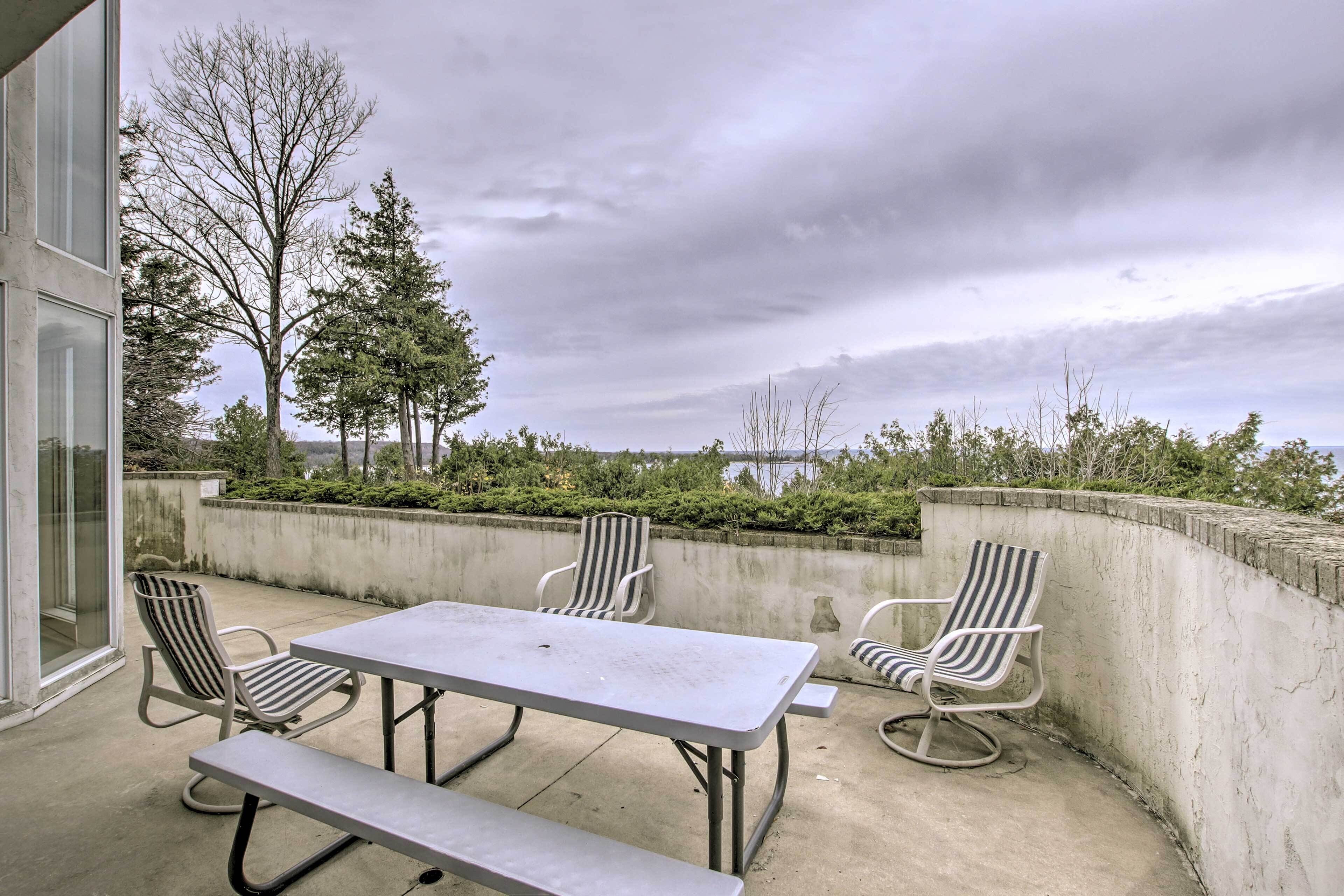 A patio with a table and four striped chairs, a bench, and a view of trees and a body of water.