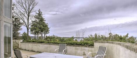 A patio with a table and four striped chairs, a bench, and a view of trees and a body of water.