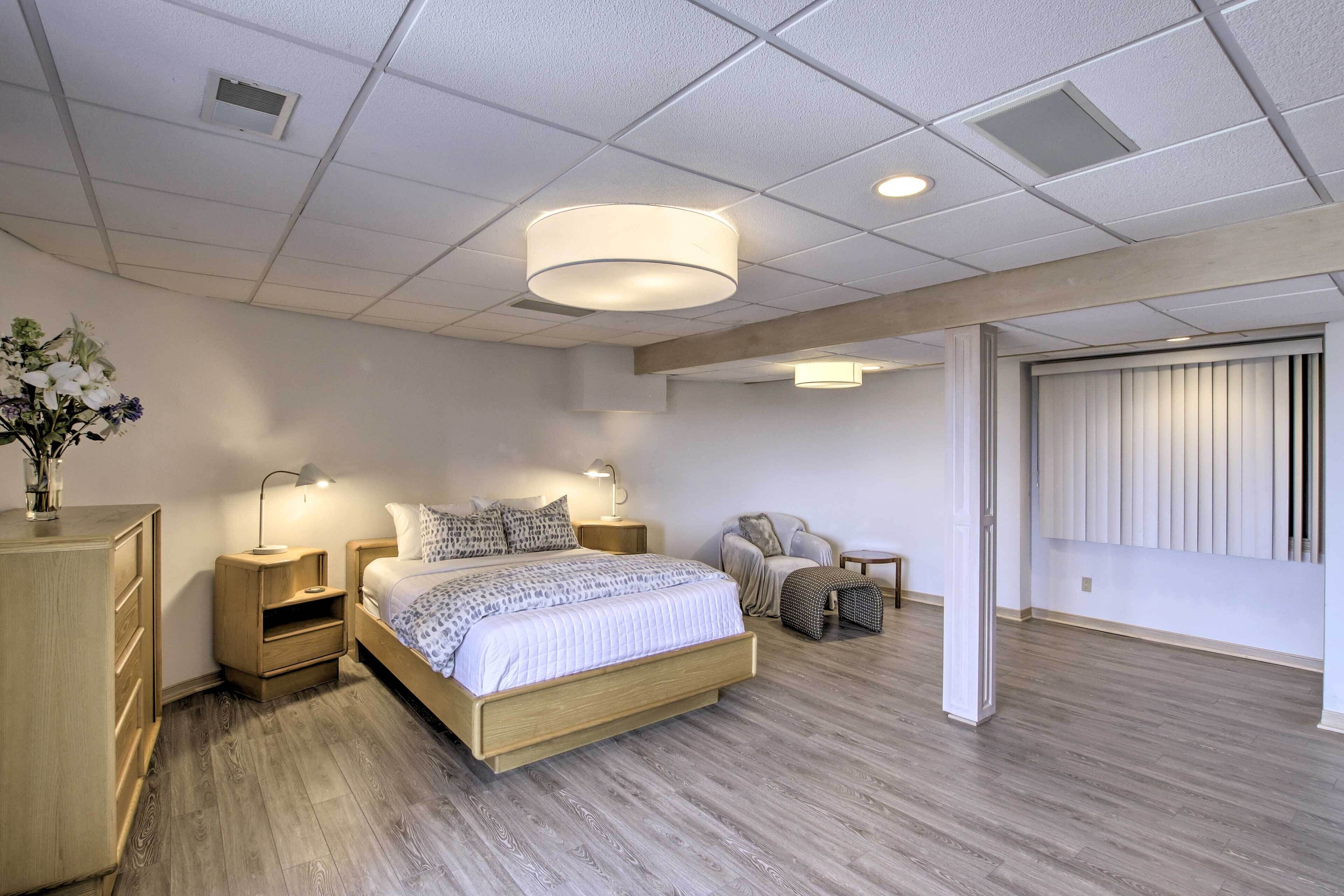 A modern bedroom with a wooden bed, bedside tables with lamps, a chair, and a large window with blinds.