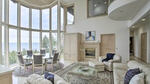 A spacious living room with a large bay window, a fireplace, and a dining area with a round table and chairs. - Grand Egg Harbor Home w/ Stunning Lake Views! (Egg Harbor)