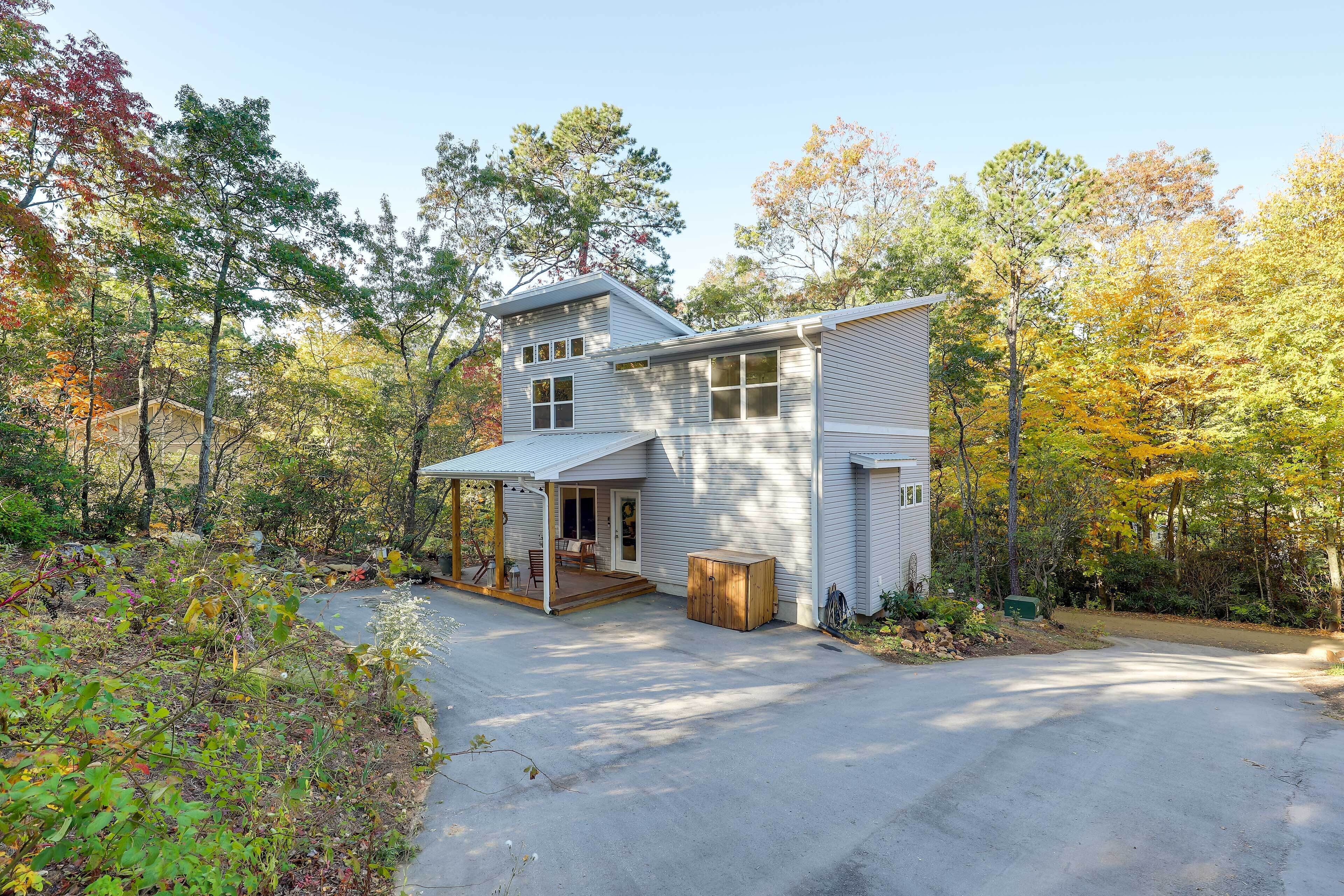 A two-story house with a covered porch and a small deck, surrounded by trees with autumn foliage.
