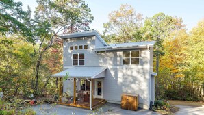 Ein zweigeschossiges Haus mit Veranda und Garage, umgeben von Bäumen und einem Garten.