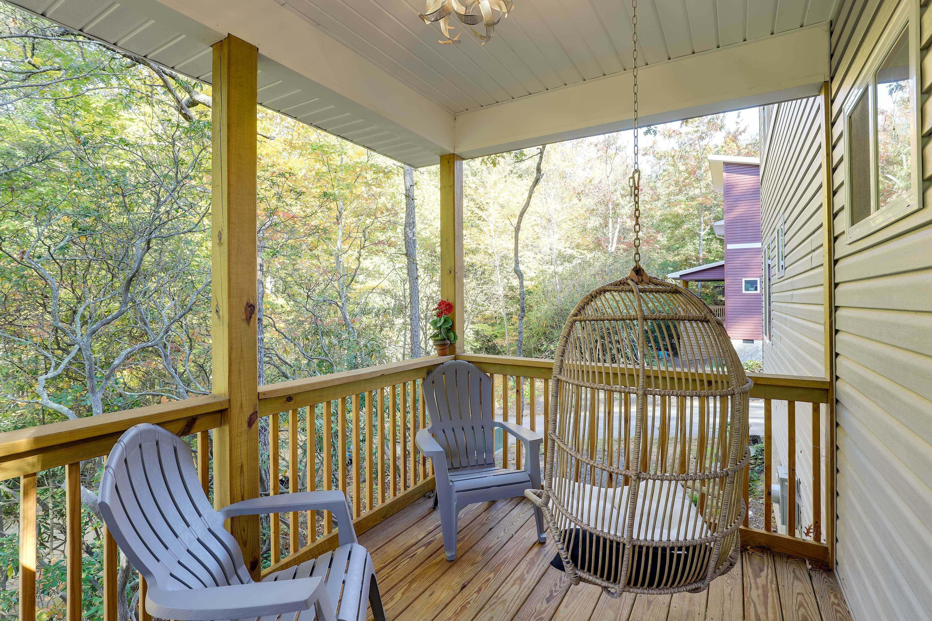 A covered porch with two Adirondack chairs, a hanging birdcage, and a view of trees and a house.