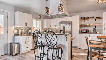 A modern kitchen with white cabinets, a stainless steel refrigerator, and a wooden dining table with two chairs.