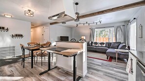 Une cuisine moderne avec un îlot central, un coin repas avec des chaises et un espace salon avec un canapé et des rideaux.