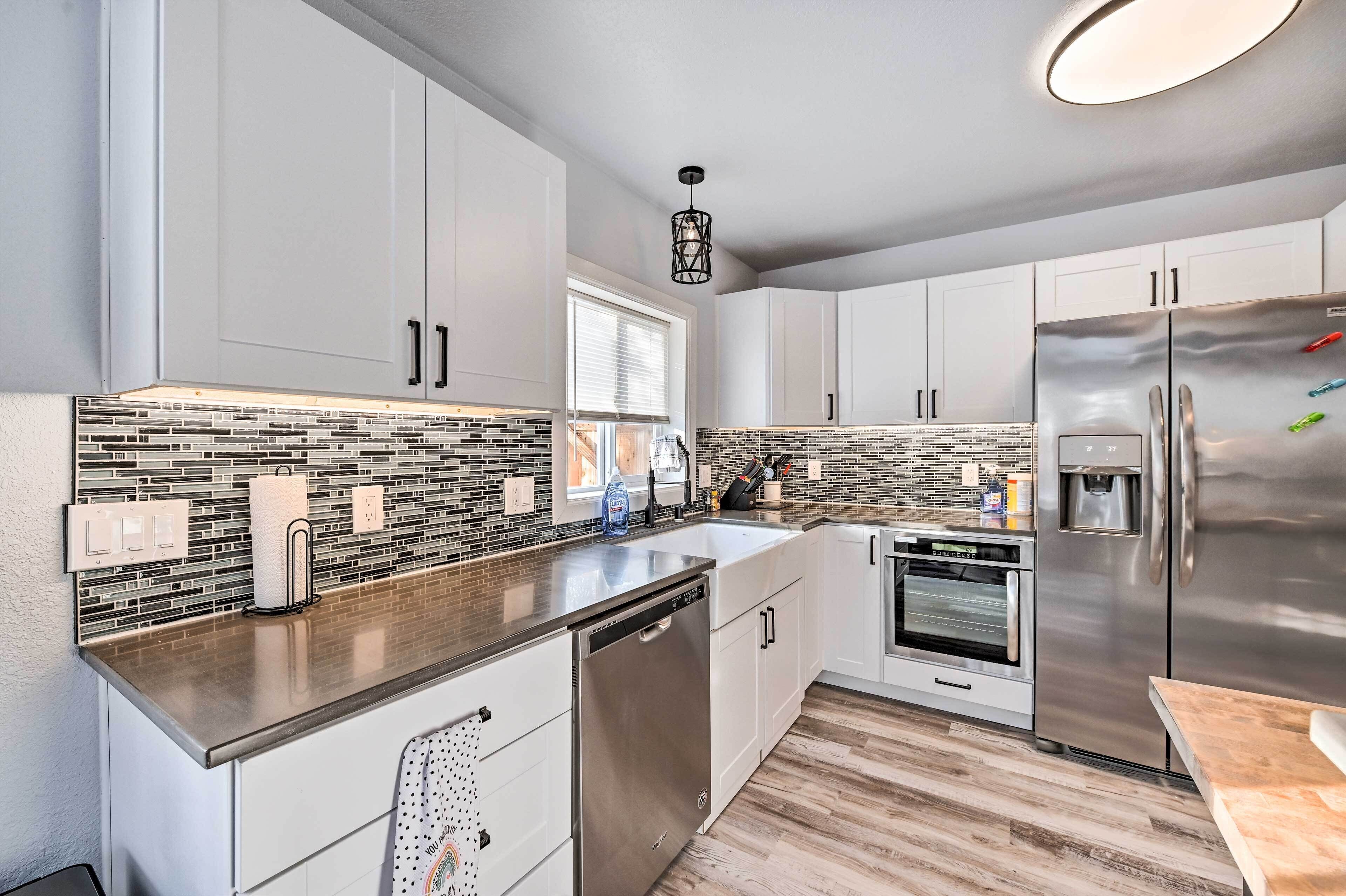 A modern kitchen with white cabinets, a stainless steel refrigerator, a dishwasher, and a tiled backsplash.