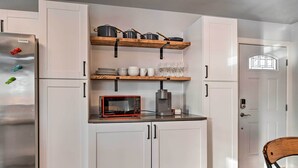 Une cuisine avec des meubles blancs, un réfrigérateur en acier inoxydable, un four à micro-ondes et des étagères où sont rangées des casseroles et des verres.