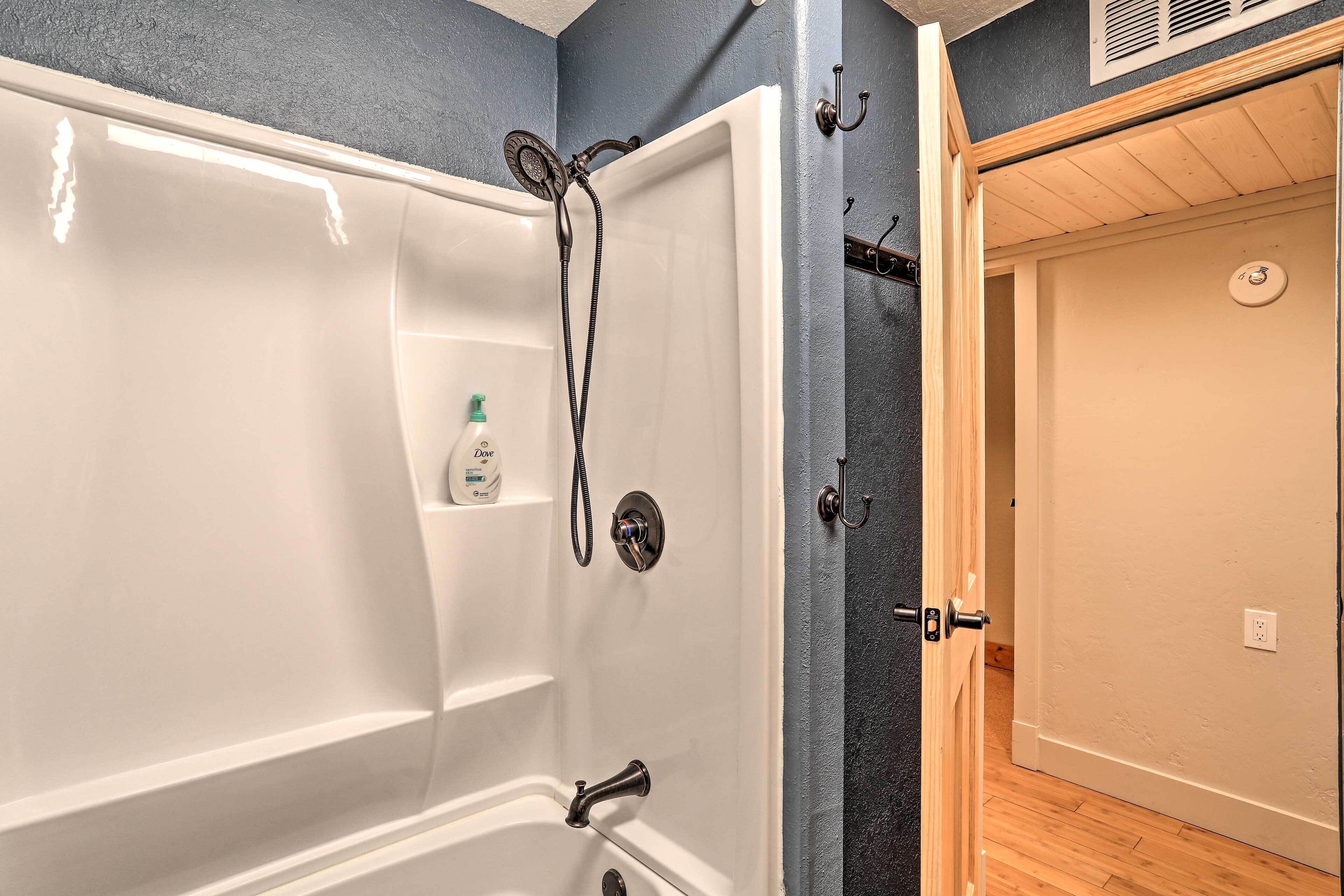 A bathroom with a bathtub, a shower, and a door leading to another room.