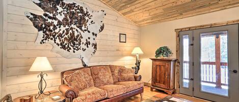 A cozy living room with a large animal hide on the wall, a leather sofa, a wooden coffee table, and a wooden cabinet.
