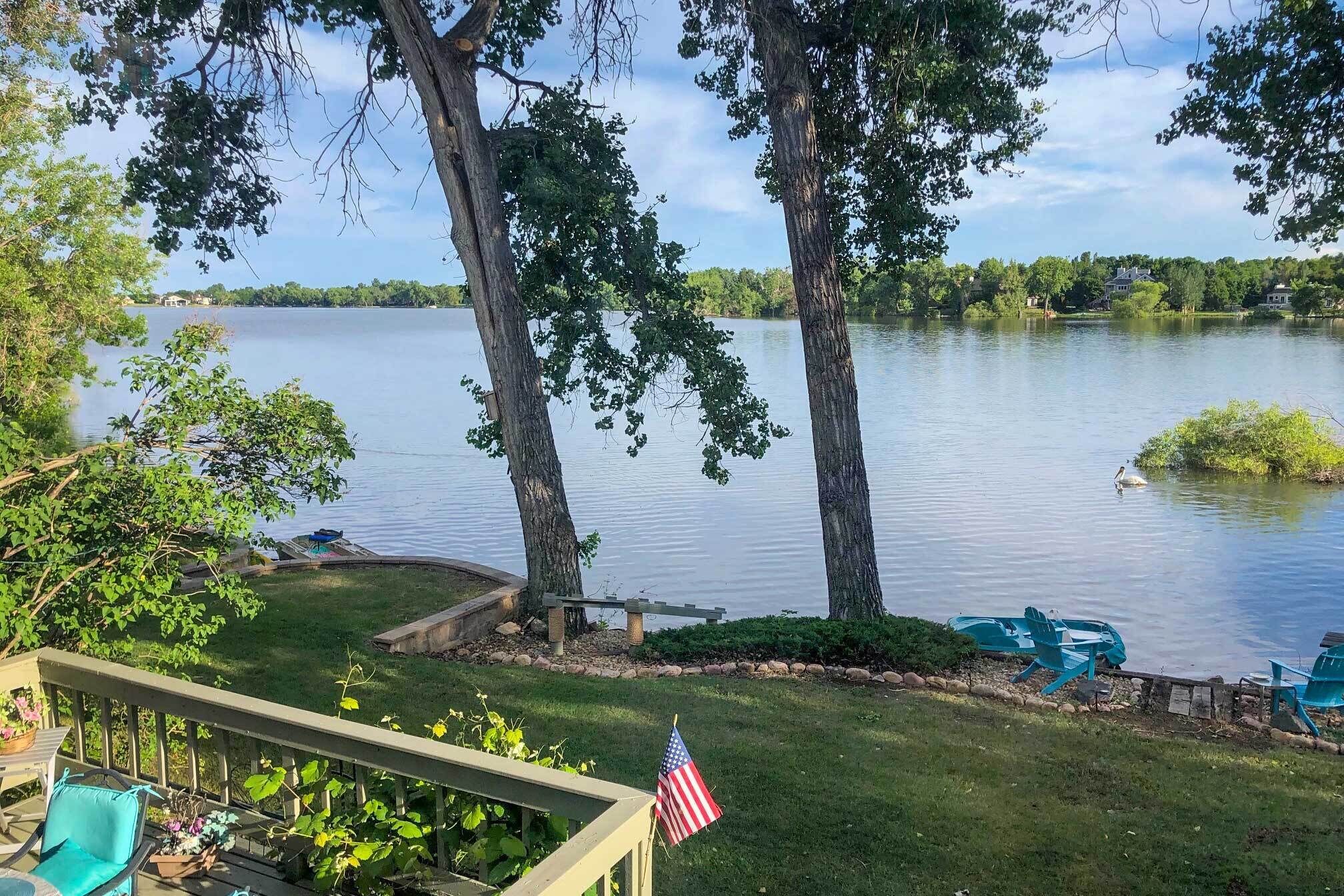 A lakeside deck with a view of the lake, a flag, and outdoor furniture.