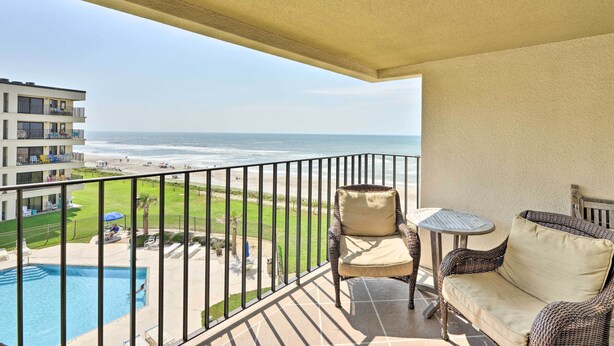 A balcony with a wicker sofa and a small table, overlooking a pool and a beach. - Summer Winds Resort Condo w/ Ocean Views! (Atlantic Beach)