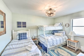 Quarto com beliches, mesa de cabeceira com abajur e janela com persianas.