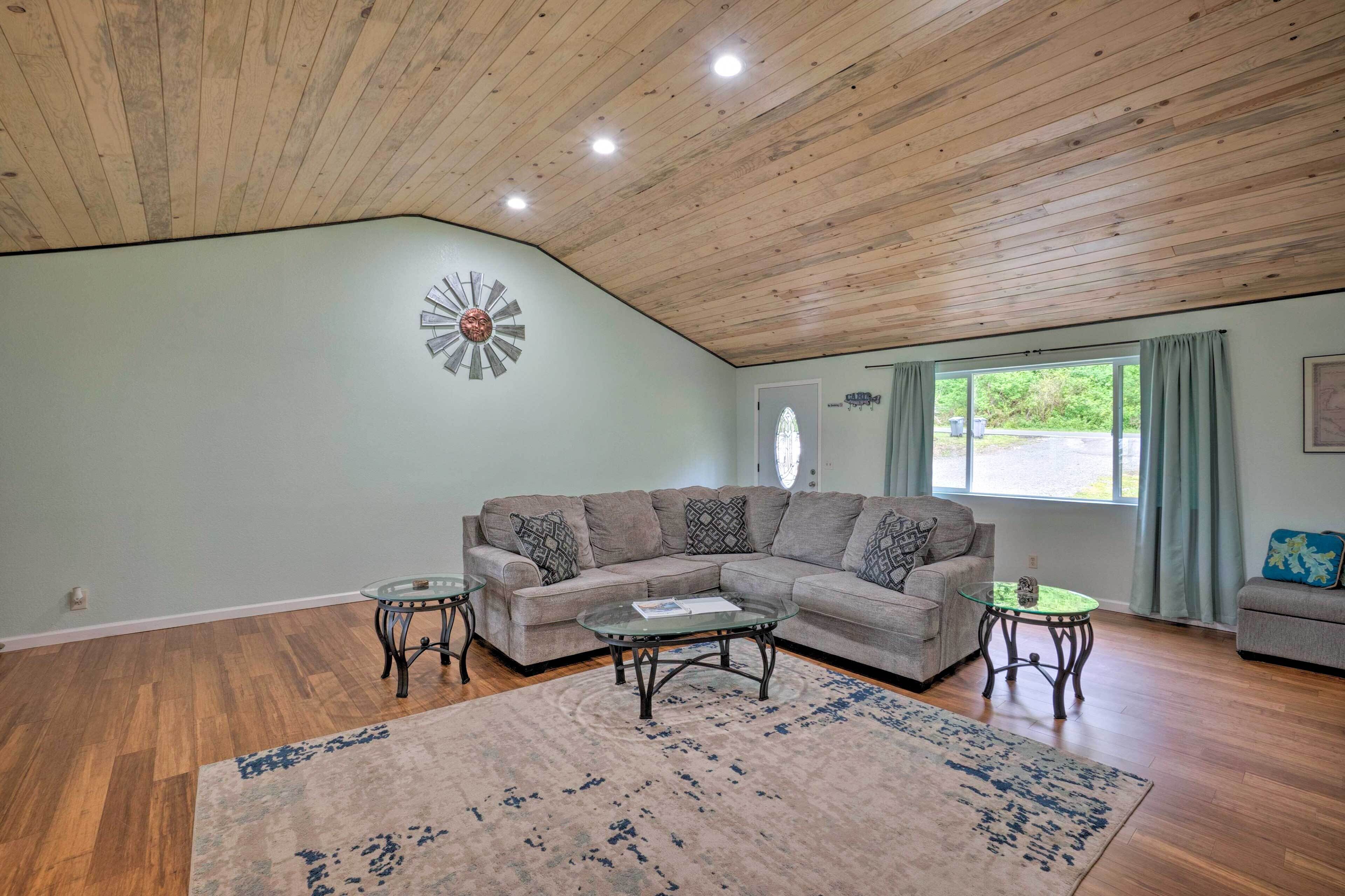 A spacious living room with a wooden ceiling, a sectional sofa, two glass coffee tables, and a large rug.