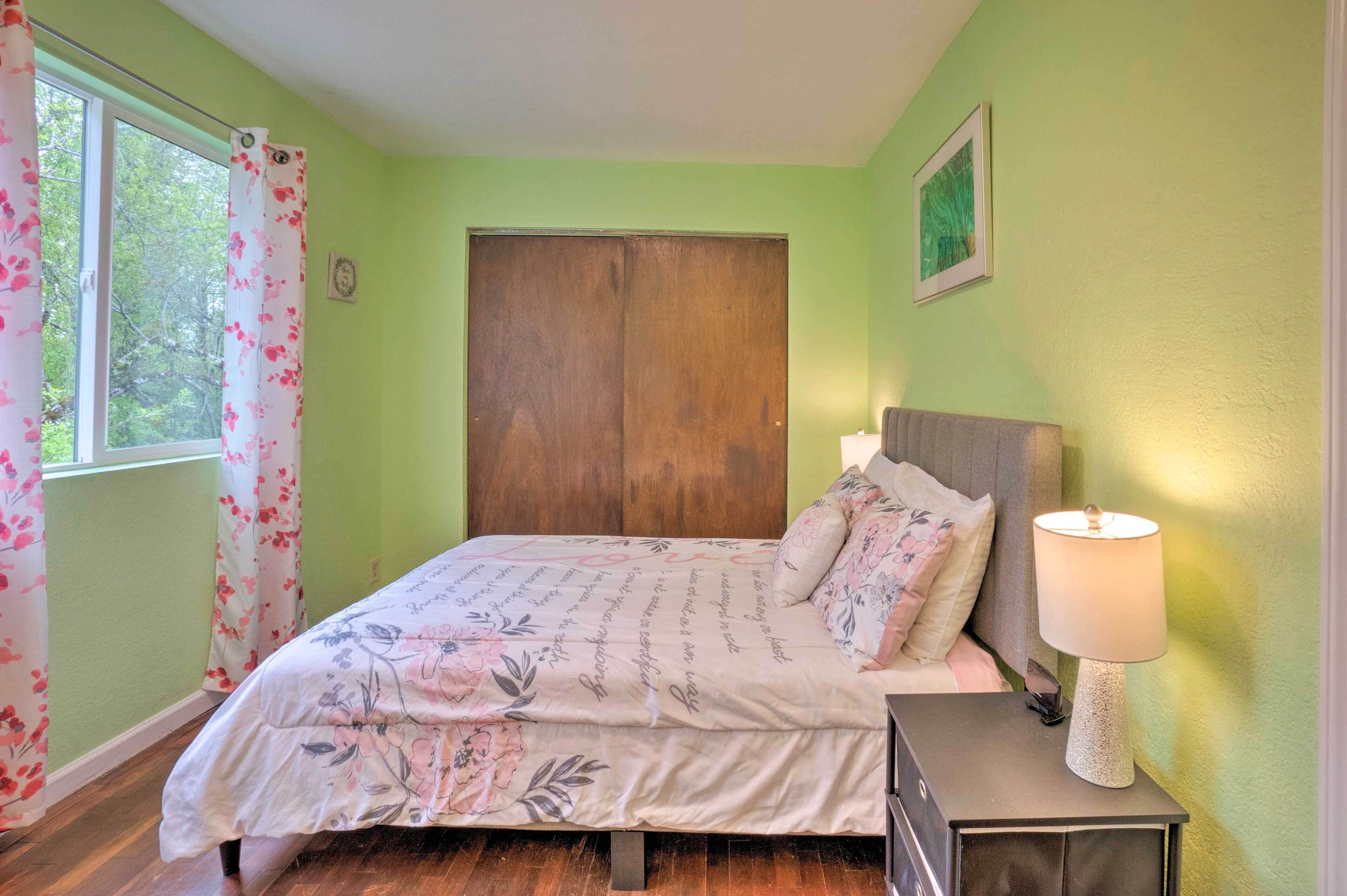 A bedroom with a bed, a nightstand with a lamp, a window with curtains, and a door.