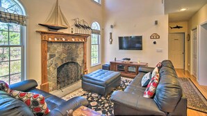 A spacious living room with a stone fireplace, leather sofas, a large television, and a view of the outdoors through large windows.