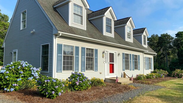 A two-story house with a gabled roof, a red door, and a small porch with a flag.