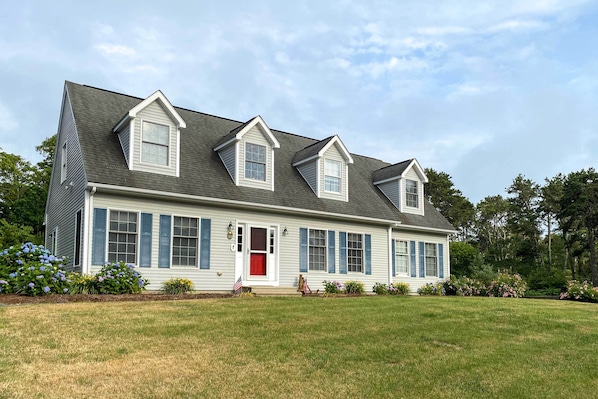 A two-story house with a gabled roof, a front porch, and a red door.
