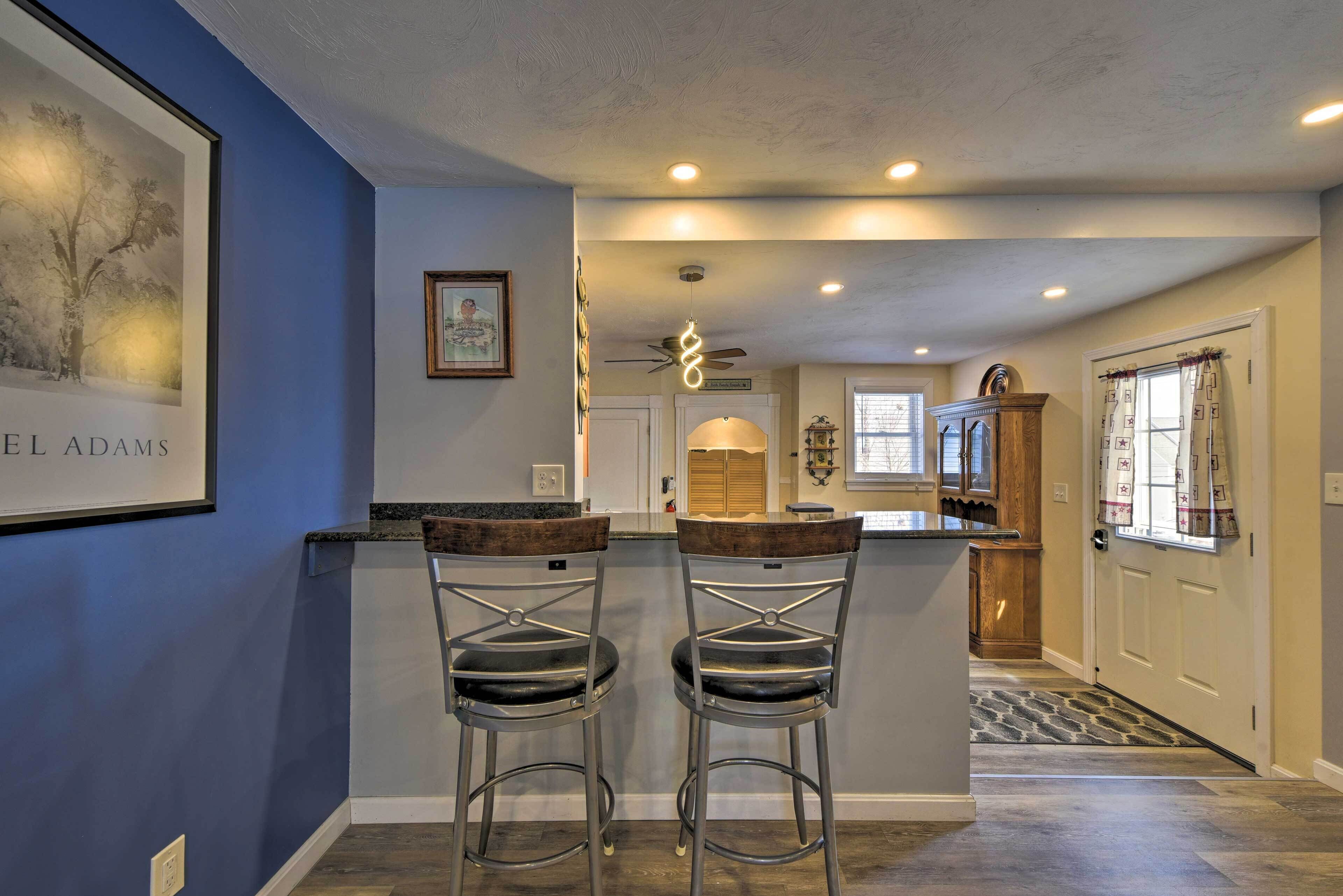 A kitchen with two bar stools, a ceiling fan, recessed lighting, and a framed picture on the wall.