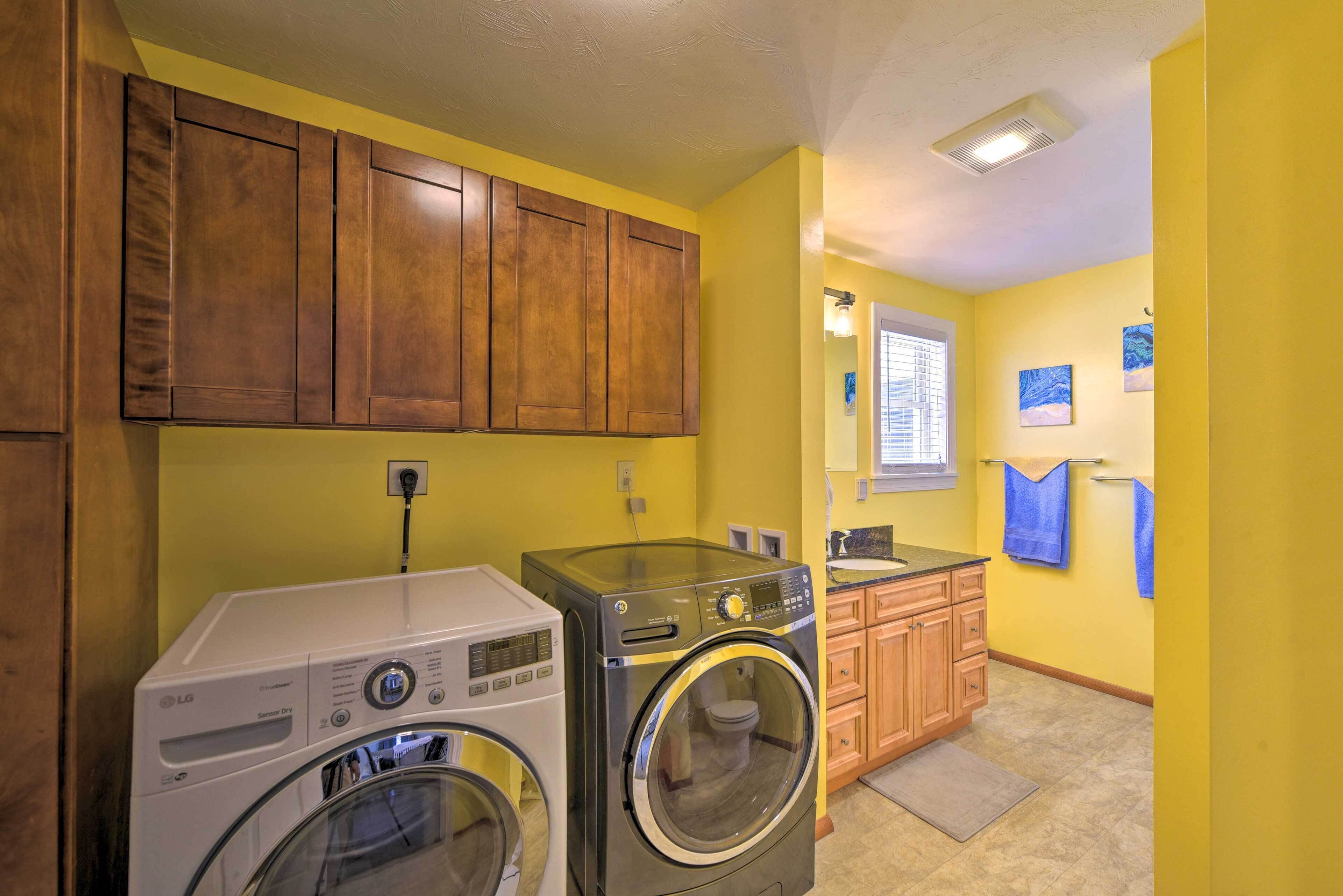 A laundry area with two washing machines, wooden cabinets, a window with blinds, and a towel rack.
