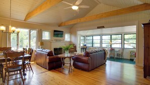 A spacious living room with wooden floors, leather sofas, a dining table with chairs, and large windows offering views of the outdoors. - Peaceful Long Pond Cottage w/ Dock & Views (Freetown)