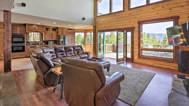 A spacious living room with a leather sectional sofa, a dining table, and a large window offering a view of the outdoors.