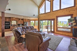 A spacious living room with a leather sectional sofa, a dining table, and a large window offering a view of the outdoors. - 2 Mi to Indian Hot Springs: Cabin in the Rockies! (Idaho Springs)