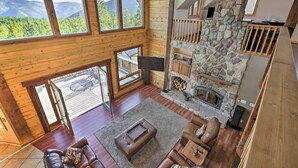 A spacious living area with a stone fireplace, wooden walls, and large windows offering mountain views.