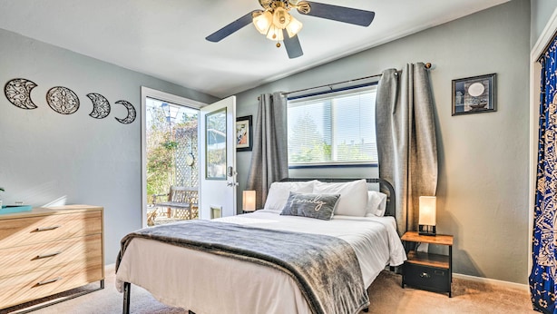 A bedroom with a bed, bedside tables, a ceiling fan, a window with curtains, and wall decorations. - Pet-friendly Eureka Home ~ 6 Mi to Old Town! (Eureka)