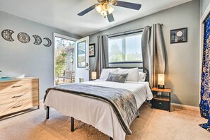 Een slaapkamer met een bed, nachtkastjes, een plafondventilator, een raam met gordijnen en wanddecoraties.