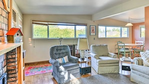 A cozy living room with a fireplace, comfortable seating, and large windows offering a view of greenery. - Pet-friendly Eureka Home ~ 6 Mi to Old Town! (Eureka)