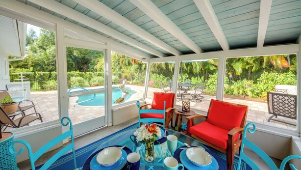 A covered outdoor seating area with a pool view, red and blue chairs, and a table with blue and white plates and cups. - Lush Punta Gorda Escape: Private Pool + Lanai (Punta Gorda)