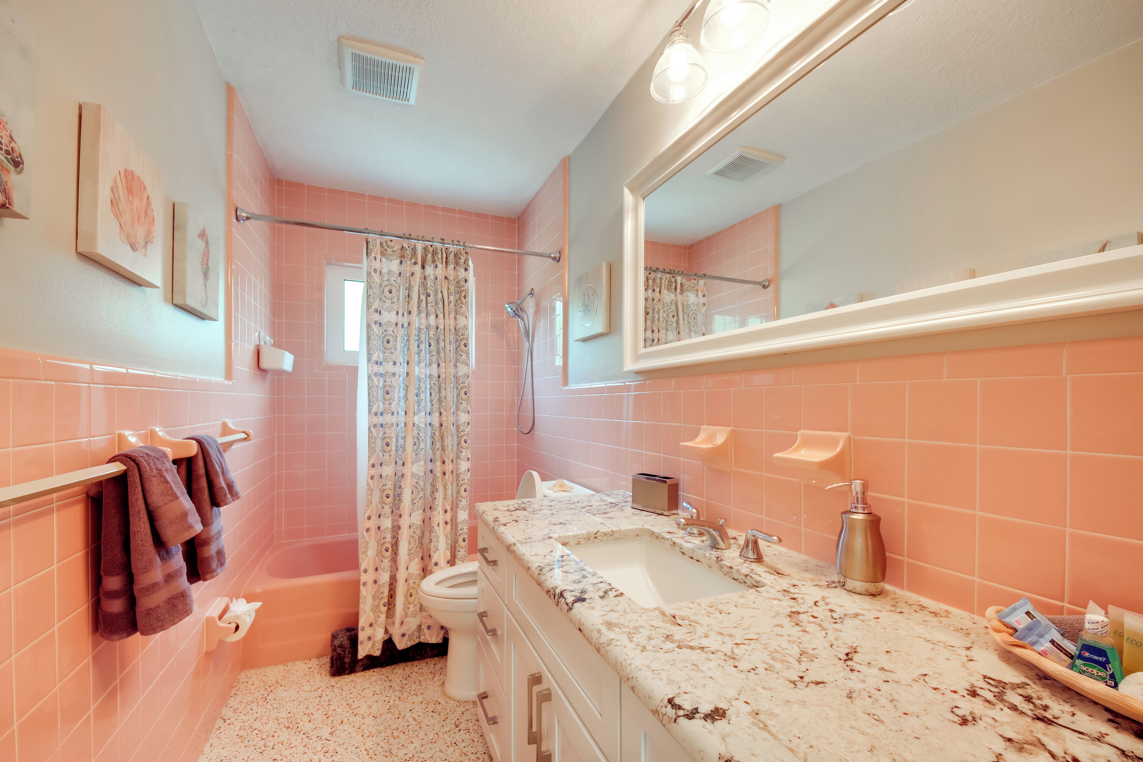 A bathroom with pink tiles, a bathtub, a sink, and a mirror.