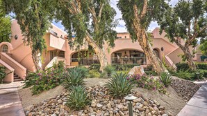 A courtyard with a stone pathway, palm trees, and a building with arches and a balcony. - Charming Palm Springs Condo By Community Pool (Palm Springs)
