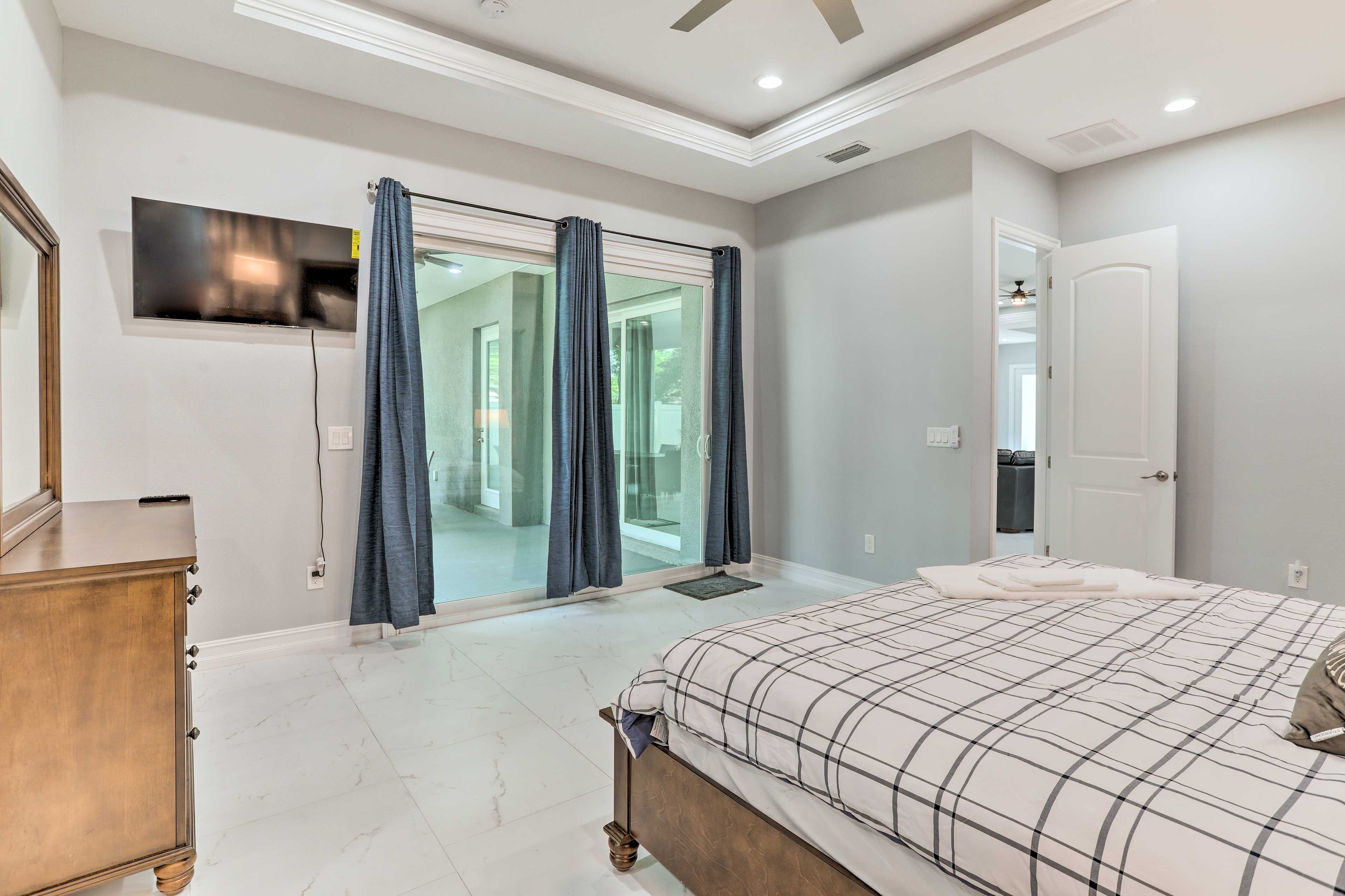 A bedroom with a large bed, a TV mounted on the wall, and a sliding glass door leading to a balcony.