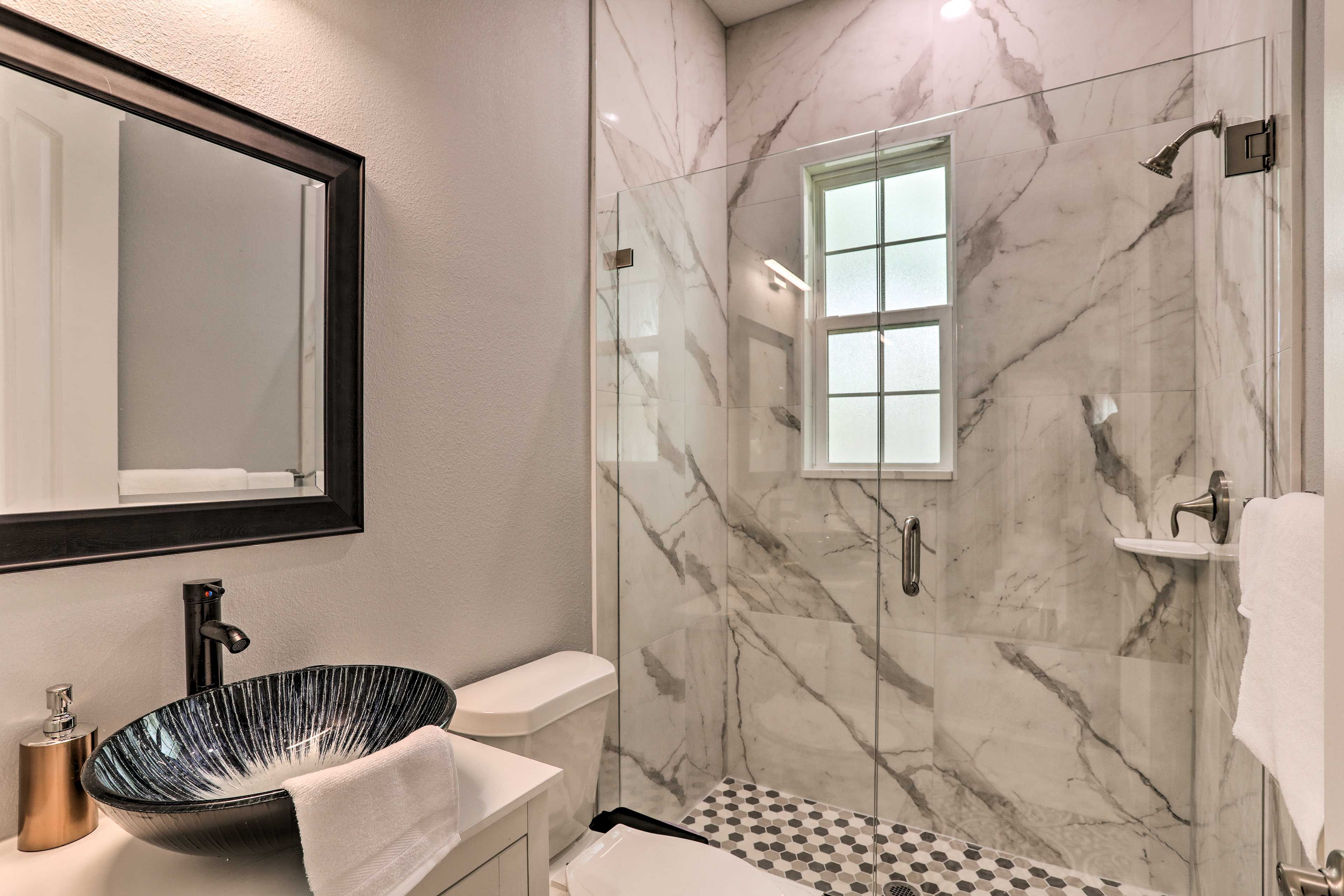 Un bany modern amb dutxa de vidre, un lavabo negre de disseny i un respatller de marbre.