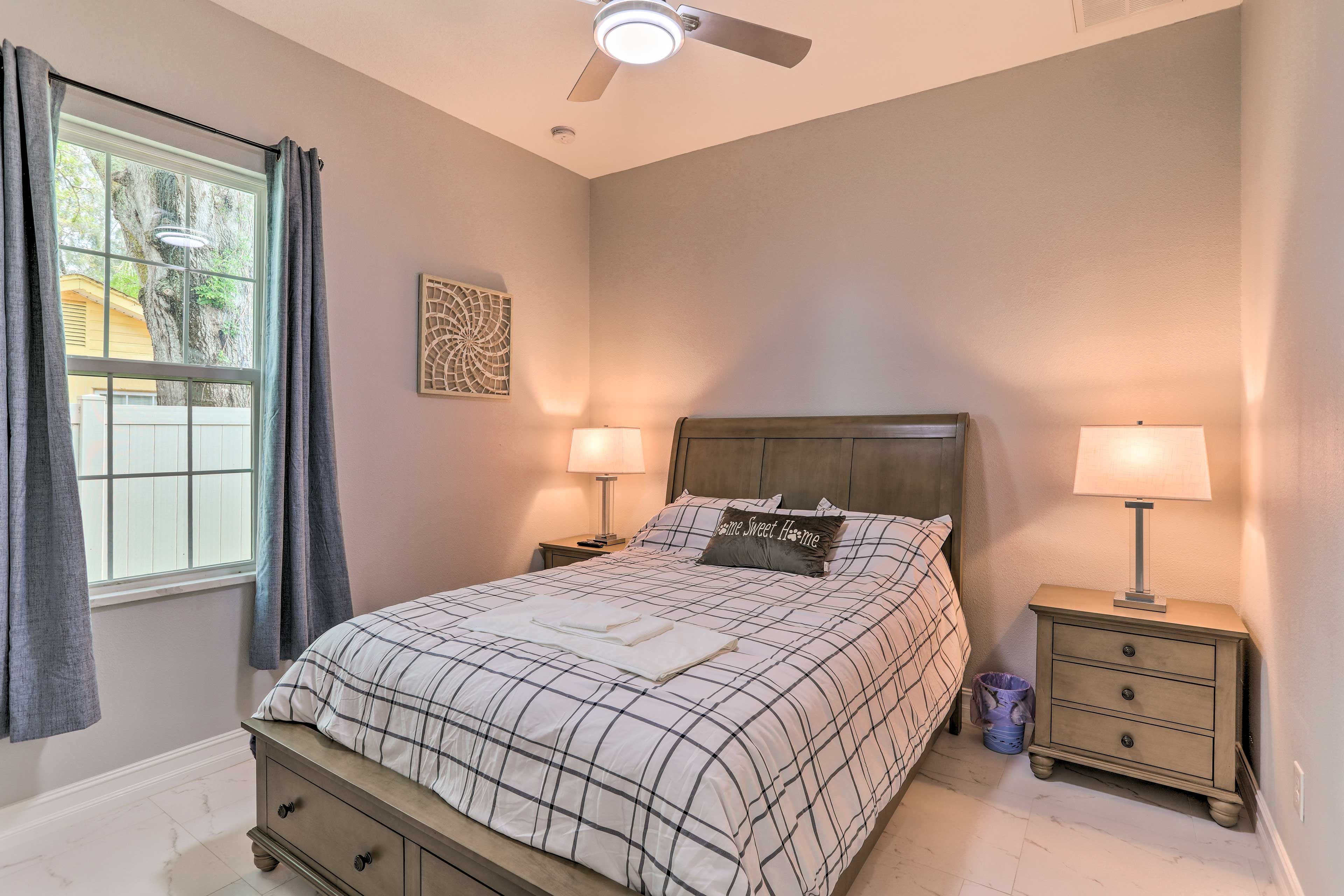 A bedroom with a bed, two bedside tables, a ceiling fan, and a window with curtains.