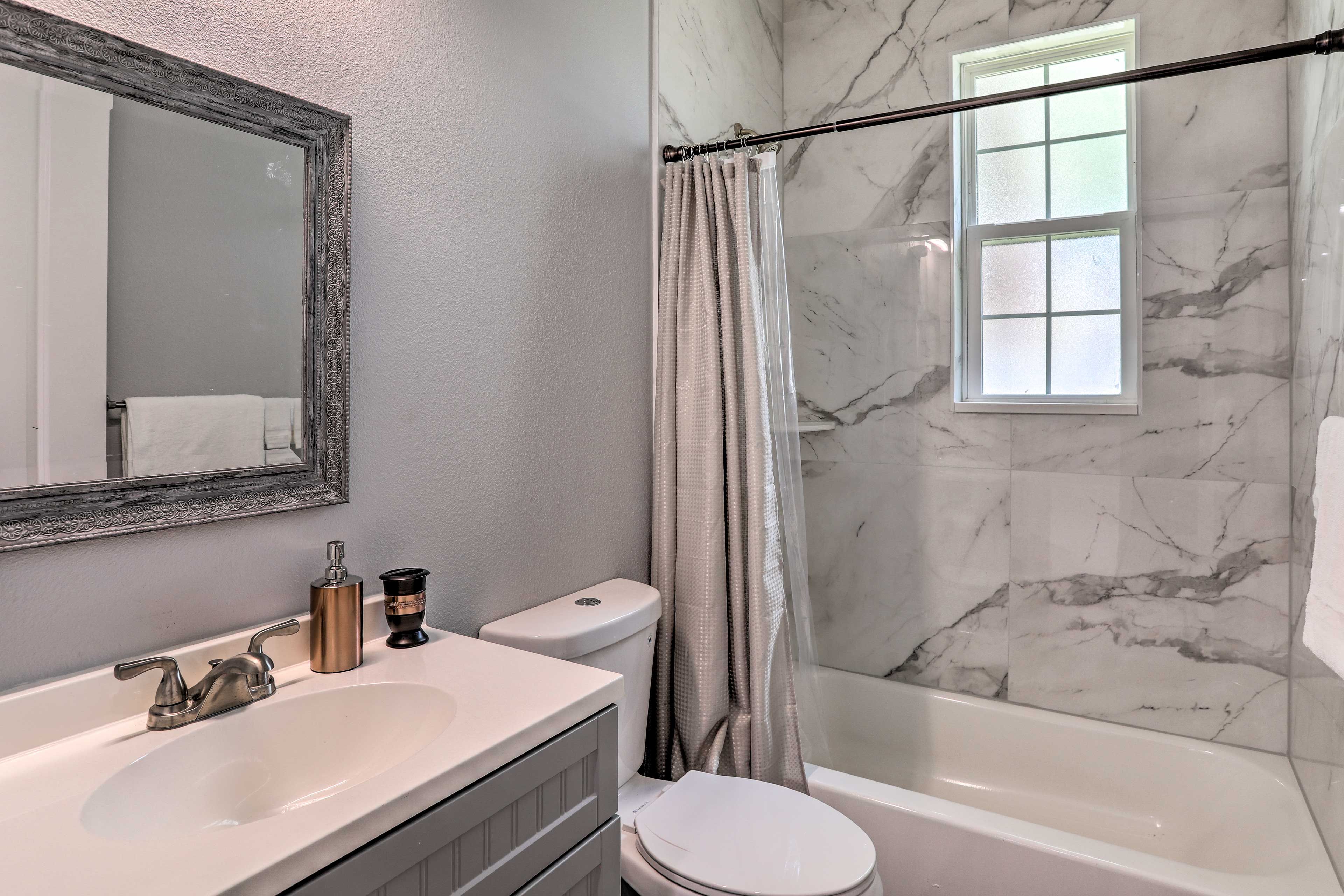 A bathroom with a marble wall, a bathtub, a toilet, a sink, and a mirror.