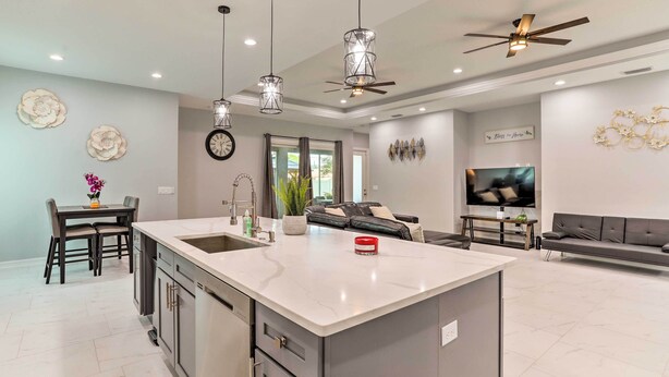 Una cocina moderna con una isla grande, luces colgantes, un ventilador de techo y un comedor con mesa y sillas.