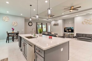 A modern kitchen with a central island, pendant lighting, and a ceiling fan.